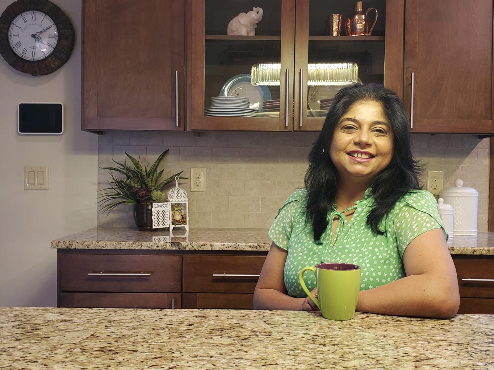 Sanchita smiling in her kitchen with a green mug of tea